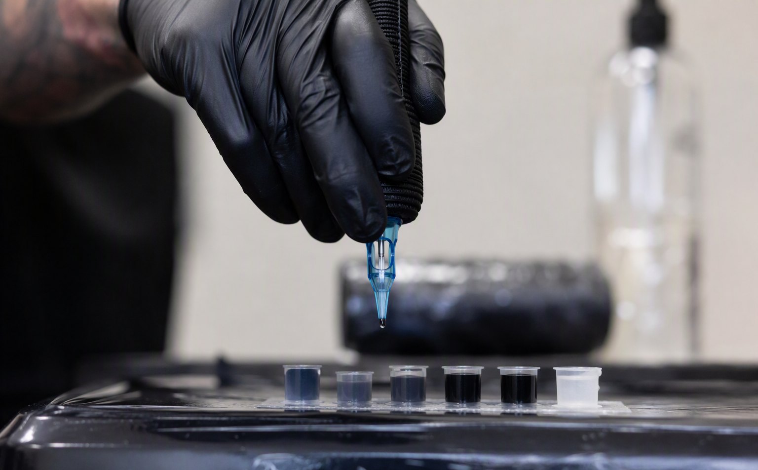 Gloved artist holding a cartridge above ink caps at a sterile workstation